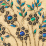 A close-up shot of a detail from a textile showing several fragments of iridescent beetle wings sewn onto the fabric.