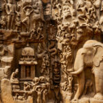 A rock-cut relief of a Hindu mythological scene with carved figures of elephants, deities and other divine beings.